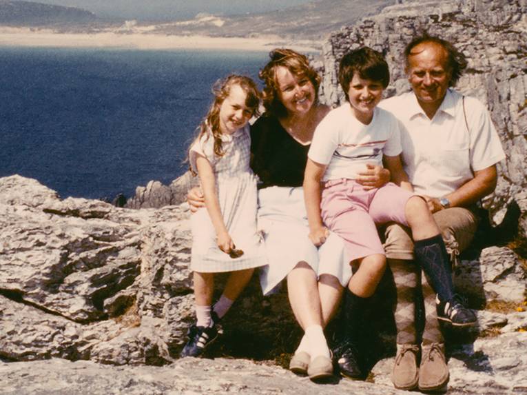 Eine fröhlich wirkende Familie, bestehend aus Eltern und zwei Kindern, lässt sich auf einem Fels fotografieren. Im Hintergrund ist das Meer zu sehen.